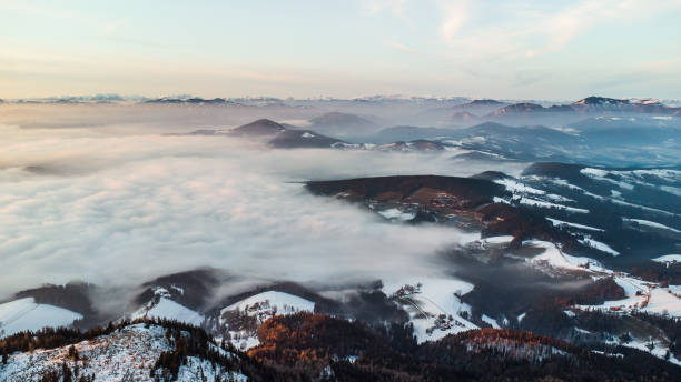 Aerial view of fog covered landscape during sunset in winter conditions. Locations is north of Graz in Austria with the village Semriach under the fog Aerial view of fog covered landscape during sunset in winter conditions. Locations is north of Graz in Austria with the village Semriach under the fog winter sunrise mountain snow stock pictures, royalty-free photos & images