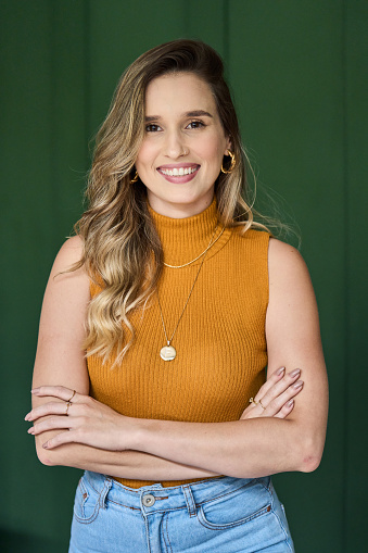 Portrait of a smiling young female architect standing with her arms crossed in front of a green wall in an office