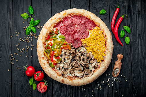 Tasty fresh pizza with four different pieces in one on wooden background. Top view of big pizza. Pizza with corn, mushrooms, pepperoni and sweet paprika