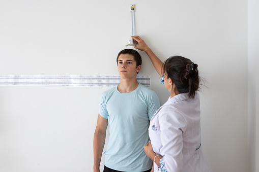 Latin american female nutritionist and deportologist at her office using anthropometric instrument to mesure height on an argentinean teenager patient. Buenos Aires - Argentina