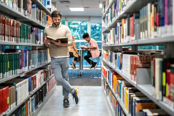 istock Mid adult man reading a book at a library 1453375271