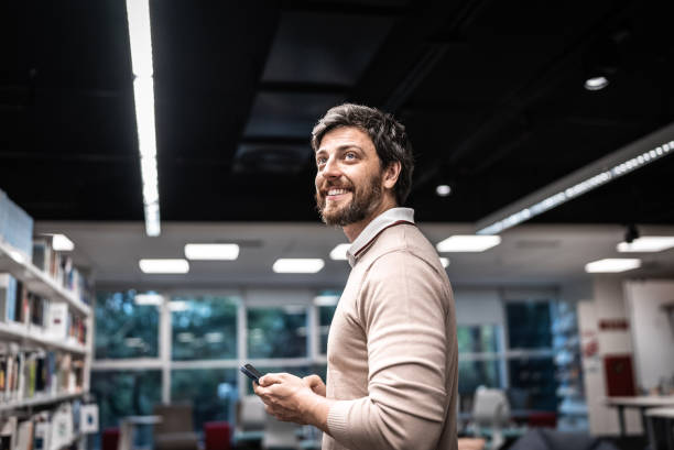 Mid adult man looking away while using mobile phone at library