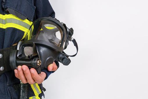 Full protective breathing mask in hand of unrecognized firefighter, rescue and fire fighter equipment isolated on gray background, copy space