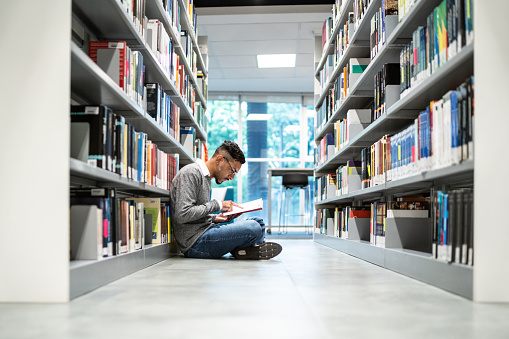 Young student man sitting on ground at the university library