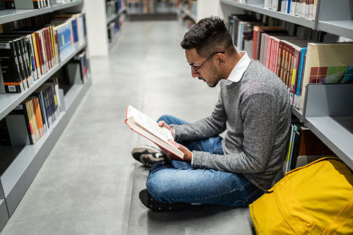 Young student man sitting on ground at the university library
