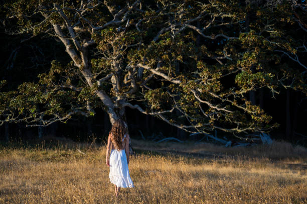A young woman is standing in a meadow by a clearing of the forest on a sunny summer day