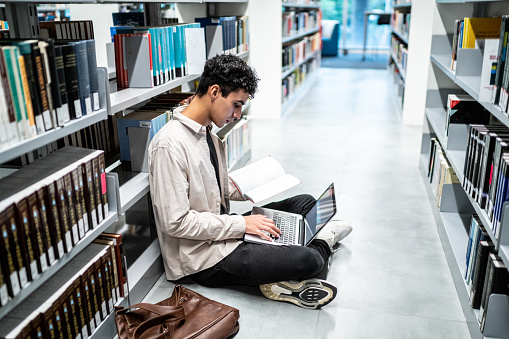 Young student man using a laptop sitting on ground at university library