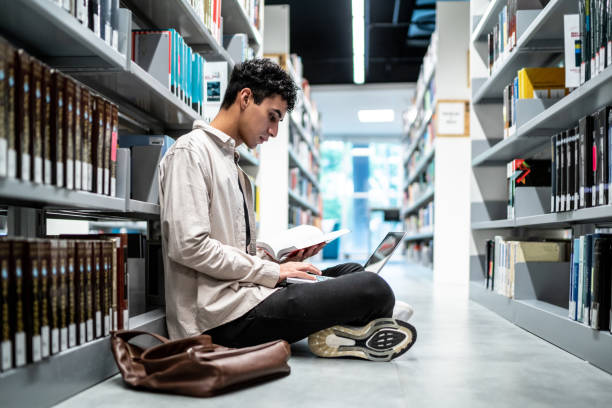 istock Young student man using a laptop sitting on ground at university library 1453382900