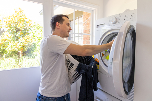 Happy man at home doing some laundry in a bright sunny room.\nPeople enjoy time off at home.