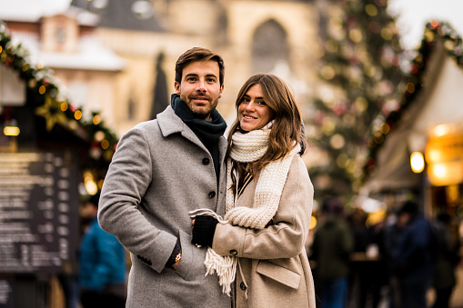 Smiling young couple looking at camera while on a walk in the city on Christmas day. They are on a Christmas market in Prague.