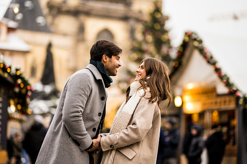 Smiling young couple embracing in the city on Christmas day. They are on a Christmas market in Prague.