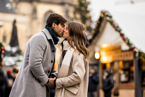 Elegant young couple holding hands and kissing in the city on Christmas day. They are on a Christmas market in Prague.