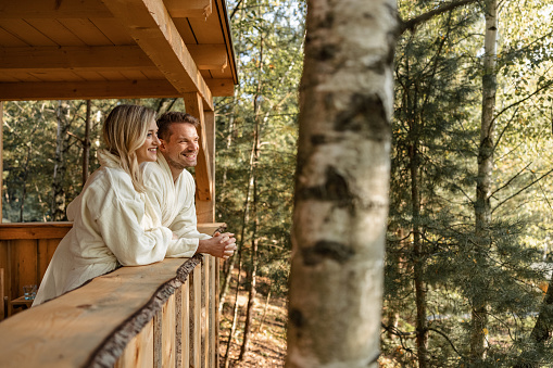 Young Caucasian couple in early 30s relaxing on patio of glamping house and enjoying the mornig view in the woods.