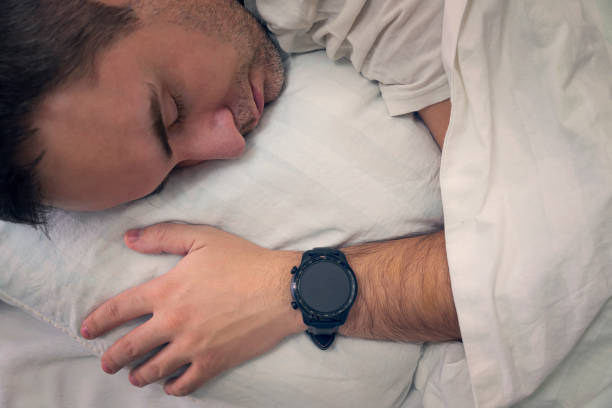 heartbeat monitoring with a smart gadget in a dream. man sleeps on a white pillow with a smartwatch on his wrist to monitor his heartbeat. a blank screen on the clock. blank smartwatch screen monitoreo de latidos del corazón con un dispositivo inteligente en un sueño. el hombre duerme sobre una almohada blanca con un reloj inteligente en la muñeca para controlar los latidos de su corazón. pantalla en blanco en el reloj. pantalla de reloj in
