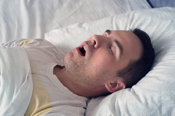 retrato de un hombre durmiendo con la boca abierta. problema de ronquidos durante el sueño. un joven lindo duerme en una cama blanca de día o de mañana - roncar fotografías e imágenes de stock
