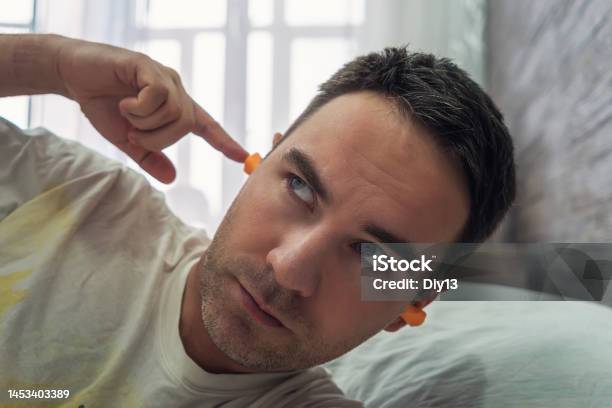 Man In His 30s Putting On Earplugs Before Sleeping Again Because Of A Noisy Morning And Neighbors A Plug In The Ears For Silence During Sleep Noisy Neighbors Interfere With Sleep Stock Photo - Download Image Now