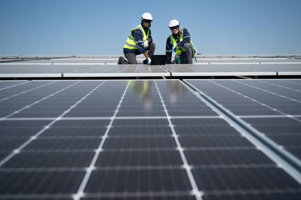 istock Caucasian and African American engineer man use electric screwdriver and computer notebook working with solar panel on roof factory 1453405630