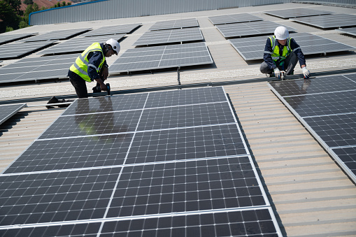 Caucasian and African American engineer man holding electric screwdriver checking solar panel on roof factory