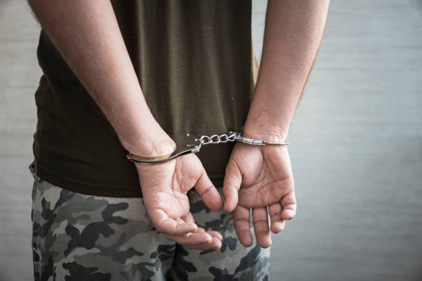 A military soldier in handcuffs, hands behind his back, on a dark background. Concept: war criminal, prisoner of war, officer tribunal. military soldier in handcuffs, hands behind his back, on a dark background. Concept: war criminal, prisoner of war, tribunal officer. detainee stock pictures, royalty-free photos & images