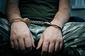 A military soldier in handcuffs, hands behind his back, on a dark background. Concept: war criminal, prisoner of war, tribunal. a prisoner of war under interrogation.