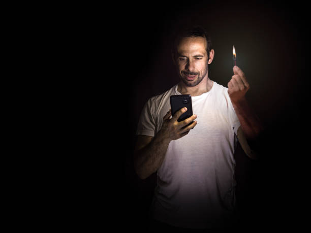 istock Man looking at his cell phone with a match in the dark. Blackout concept. Selective focus. 1453409241