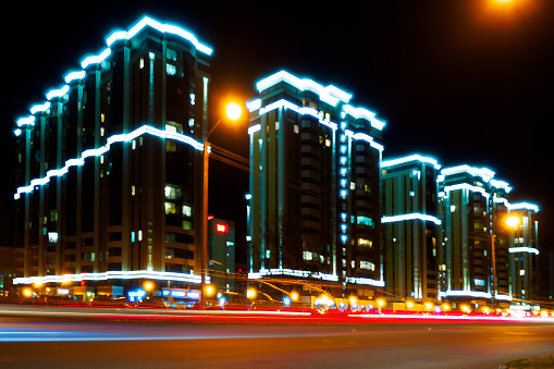 Night city. Photo with motion blur effect. Modern residential multi-storey house with illumination. urban infrastructure. Glow-in-the-Dark Luxury Residential Complex Beautiful Background..