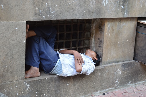 MUMBAI, India – September 09, 2022: A homeless man takes a nap on an empty air conditioner slot in Mumbai, India