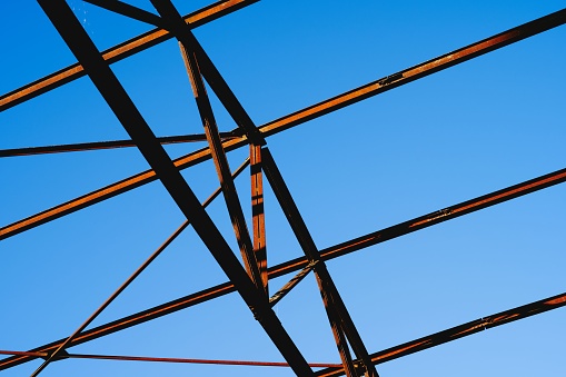 A low-angle shot of the steel truss and purlin of a building under a beautiful blue sky