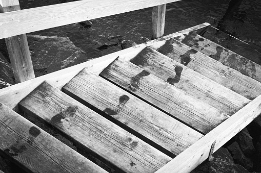 A grayscale shot of Wet footsteps on wooden stairway over lake water