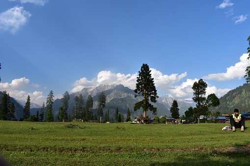 Arang kel, Pakistan – June 16, 2022: A view of a male sitting on the grass on the background of trees and mountains in Kashmir, Pakistan