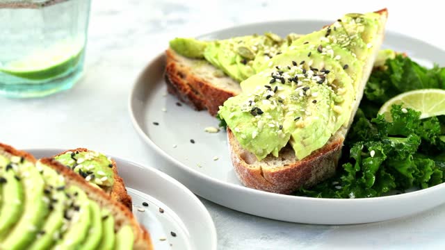 Tasty avocado and toast with sesame seeds, lettuce, and lime on a white plate