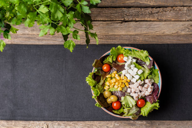 istock Plate with vegetable salad, corn, tomato, olives, turkey and cheese, on a gray tablecloth on a rustic wooden table, with parsley garnish, copy space. 1453427676
