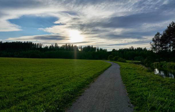 istock Curving dirt trail on the side of a grass field under a cloudy blue sky 1453432111