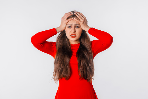 Portrait of the shocked anxious young woman in panic, holding hands on head and worrying, standing frustrated and scared against white studio background. Psychology, depression, bad mood, stress