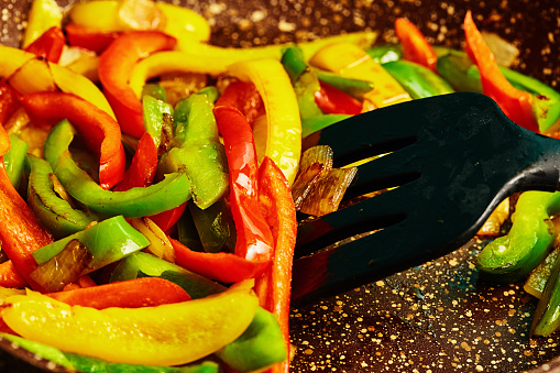 Healthy fry-up: multi colored bell peppers in frying pan being stirred with spatula.