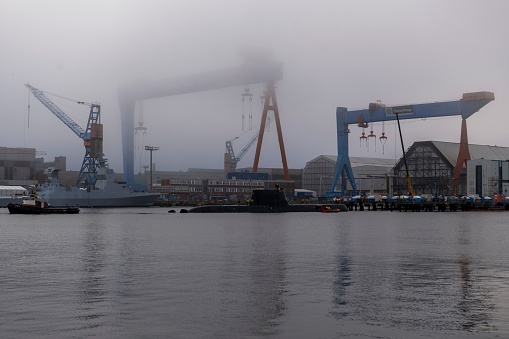 Ships and cranes on sea at shipyard against sky in city during foggy weather