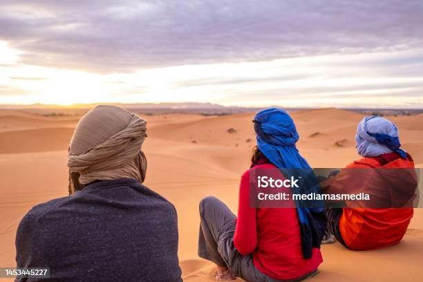 Three Adventure Traveler Friends Watch The Sunset From A Dune In The Sahara Desert A Trip With Friends Strengthens The Friendship And Improves The Level Of Trust And Closeness Stock Photo - Download Image Now