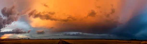 Panoramic photo of a departing thundercloud, illuminated orange by the light of the setting sun