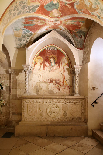 Trani, Province of Barletta-Andria-Trani, Italy - 29 december 2022: Cathedral of San Nicola il Pellegrino - lower church of Santa Maria della Scala: to the right of the altar is the sepulcher of Passapepe Lambertino from the 15th century, with a sarcophagus carved with heraldic coats of arms. Frescoes decorate the space under the tabernacle and the sails of the vault that precedes the monument.