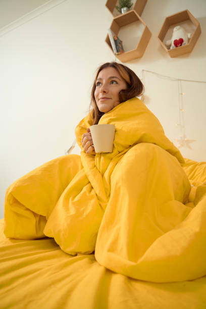 istock Smiling female daydreaming in bed with cup in hands 1453453747