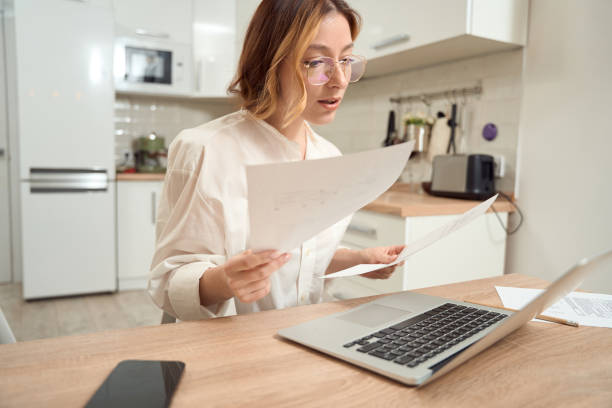 istock Concentrated lady with papers sitting at portable computer 1453453838