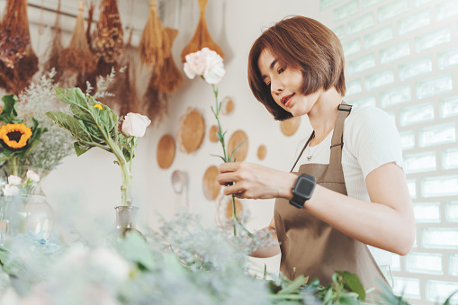 Pretty Asian Korean woman Florist in apron cutting bouquet of flowers in flower shop, Making decorations and arrangements flowers, Small business, Entrepreneur