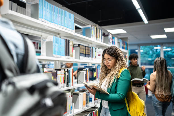 giovane studentessa che legge un libro alla biblioteca universitaria - library student latin american and hispanic ethnicity university foto e immagini stock