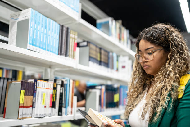 istock Young student woman reading a book at university library 1453463970
