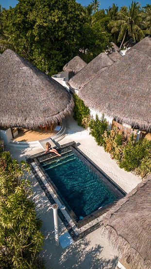 Woman sitting by swimming pool in Maldives hotel beach villa on tropical island resort aerial drone view