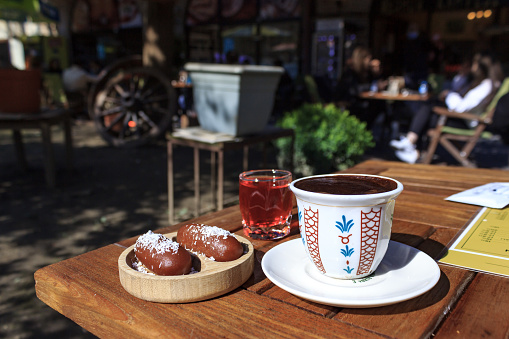 Cup of Turkish coffee with traditional dessert and sherbet on wooden table in outdoor cafe. Turkish food culture.