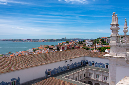 View over Lisbon with the courtyard at the church of São Vicente de Fora in the foreground. Richly decorated with azulejos tiles.\nIn the distance the The Ponte 25 de Abril over the Rio Tejo can be seen.