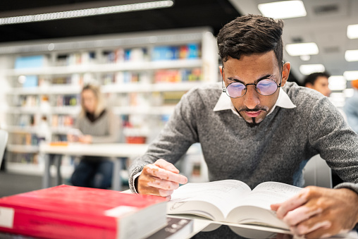 Young student man reading a book at university library