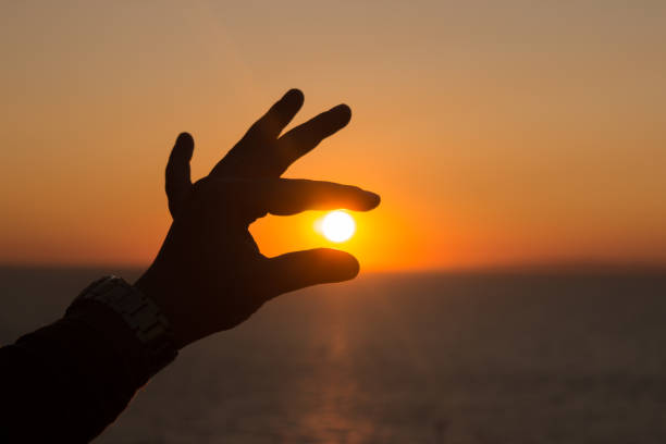 istock Woman hand silhouette catching the sun at sea and sunset landscape 1453465708