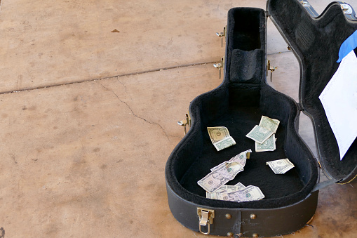 Street performer’s open guitar case with donations